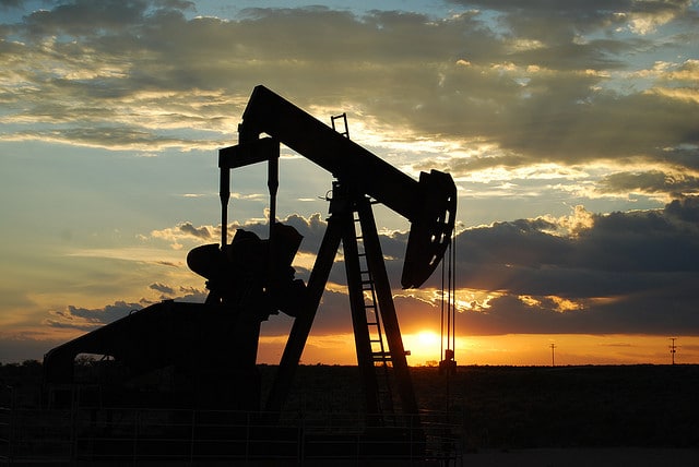 An oil pumpjack seen in profile as sun sets.