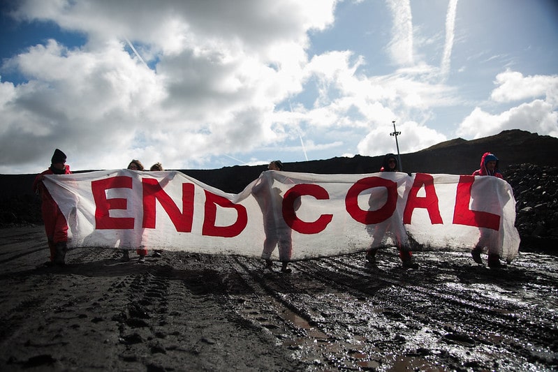 Activists hold a white banner with red letters reading "End Coal"