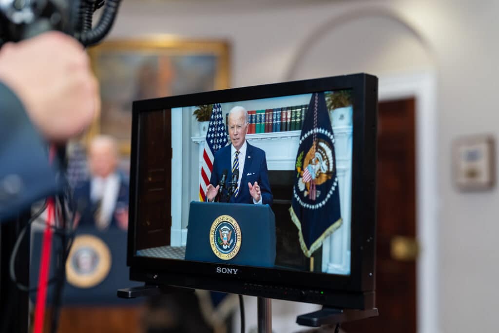 View of monitor showing President Biden at a podium with US flag and seal