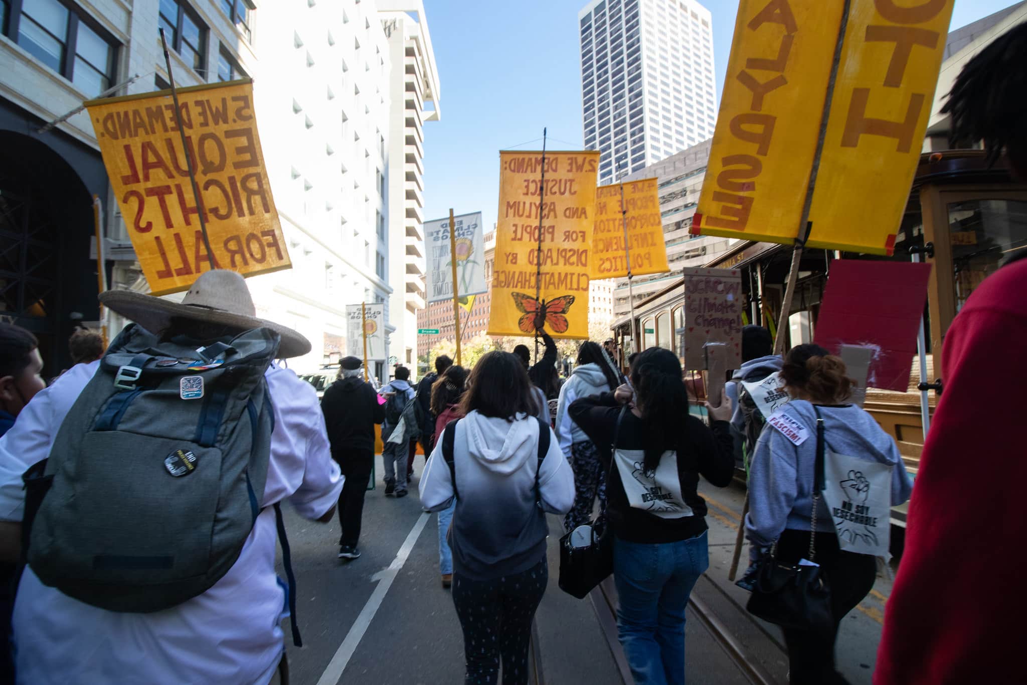 Protesters march in a street, carrying yellow signs