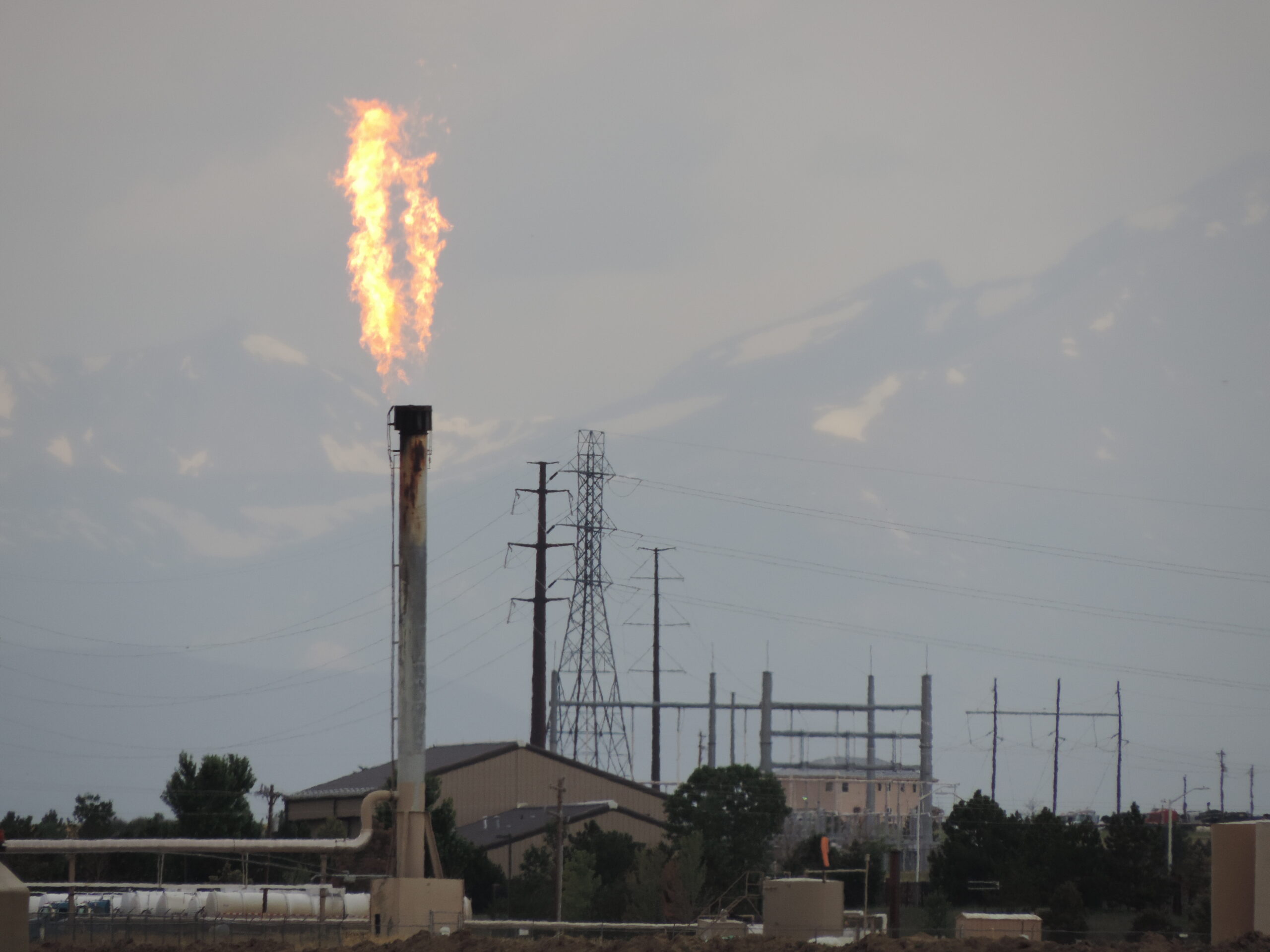 a photo of a gas flare in the foreground and snowy mountains in the background