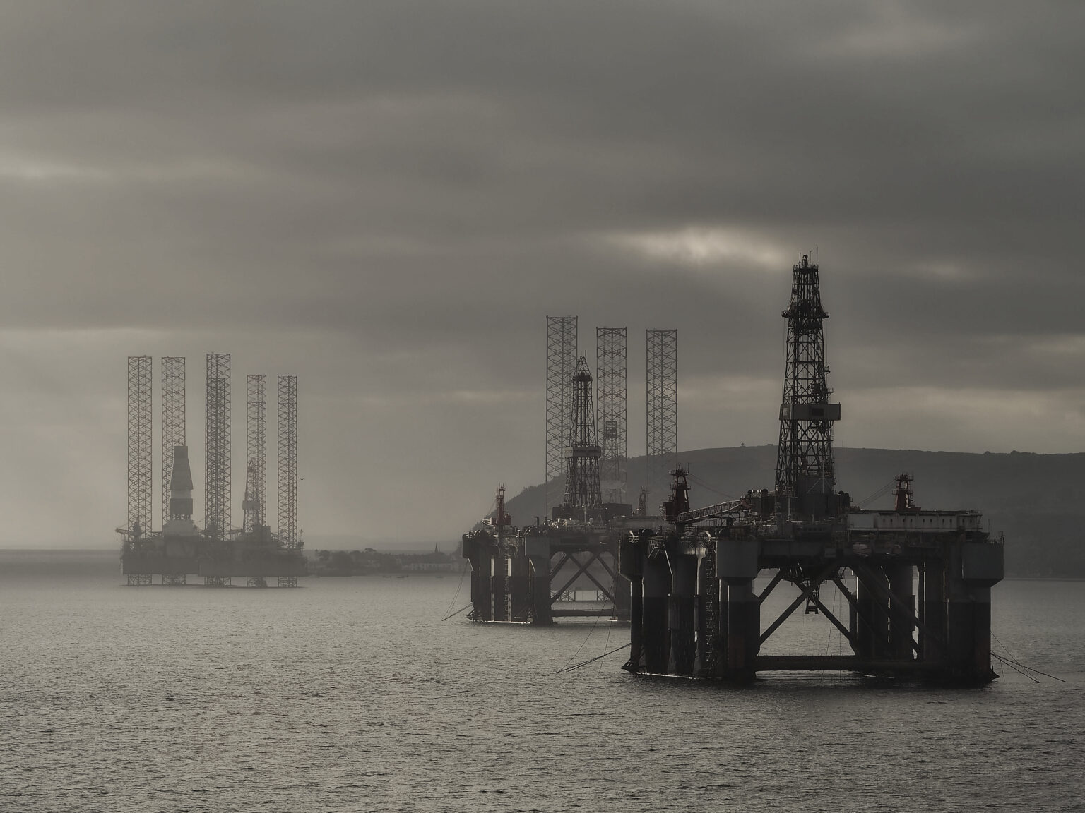 This atmospheric photo in shades of black and white shows oil platforms rising from the sea amid clouds.