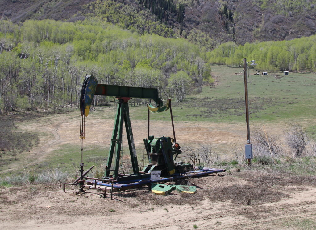 A low-producing or inactive pumpjack in Colorado surrounded by green scrub and hills.