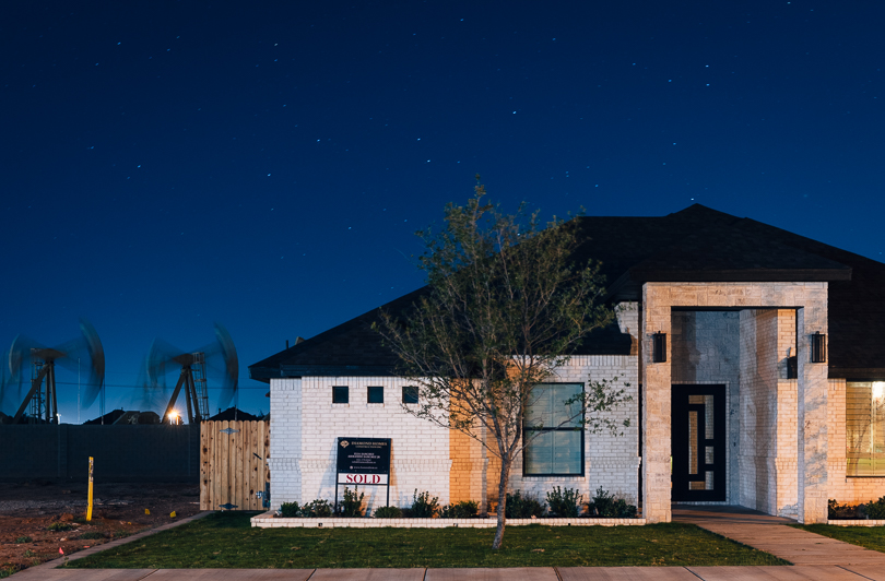 A new house for sale next to an active oilfield in Midland, Texas, with stars in the night sky.