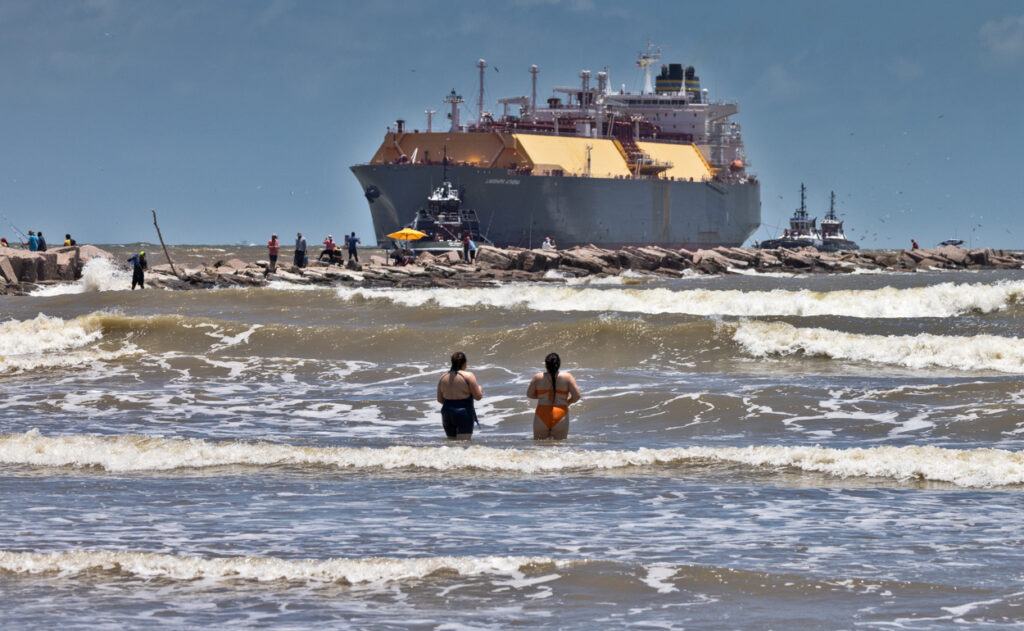 LNG tanker with swimmers in the surf at Freeport Beach, Texas.