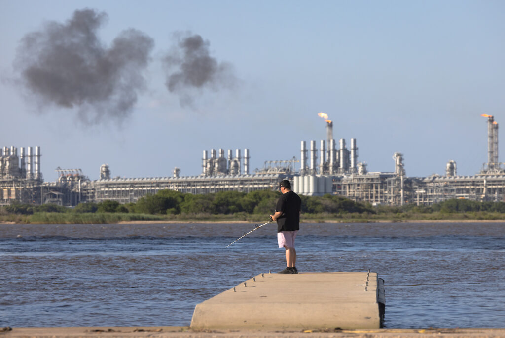 Man fishing on the Texas side of the Sabine Pass, across from Cheniere's LNG export facility as it flares from smokestacks.