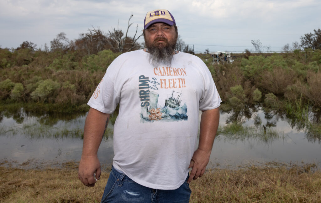 Travis Dardar standing in front of a marshy area and damaged home.