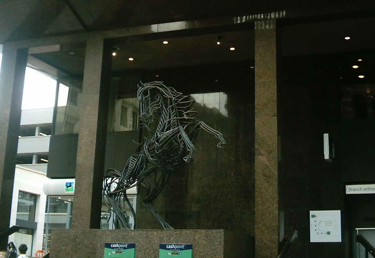 Large metal sculpture of a black horse outside an impressive office building.